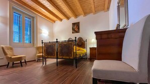 Ein Schlafzimmer mit Holzbalkendecke, einem Bett mit Holz Kopfteil, einem Nachttisch, einem Sessel und einem Sofa.