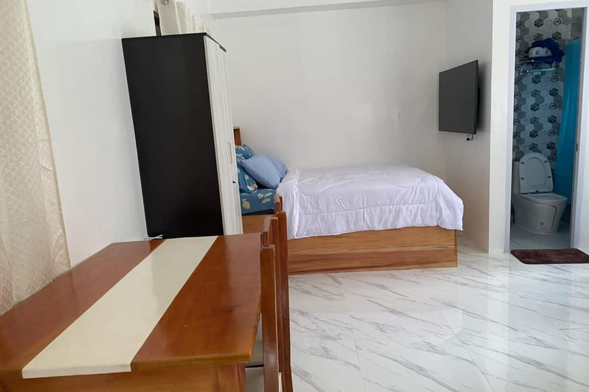 A room with a bed, a TV mounted on the wall, and a bathroom visible through an open door.