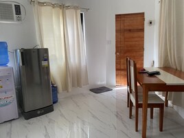 Una cocina compacta con refrigerador, dispensador de agua y una mesa de comedor de madera con sillas.