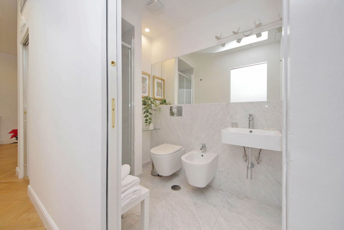 Un bagno moderno con WC, bidet e lavandino, caratterizzato da pareti in marmo bianco e un grande specchio.