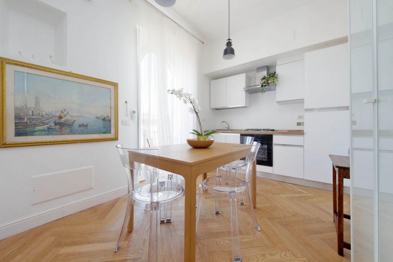 Eine moderne Küche mit weißen Schränken, einem Holztisch mit klaren Stühlen und einem Bild an der Wand.