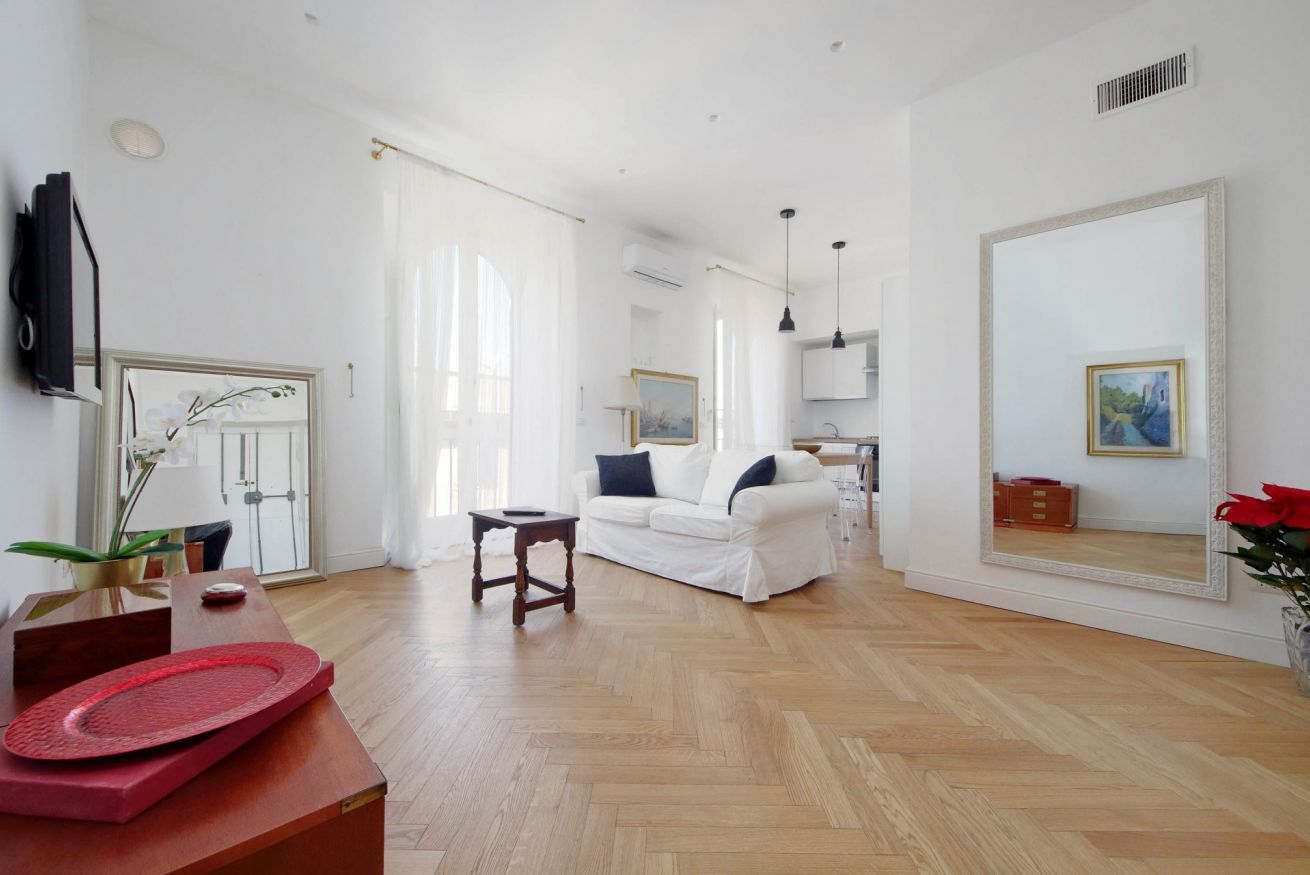 A spacious living room with a white sofa, wooden flooring, and a large mirror.