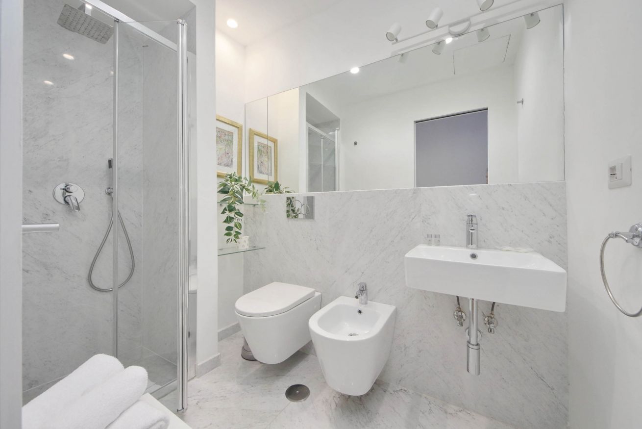 A modern bathroom with a glass-enclosed shower, a bidet, a sink, and a mirror.