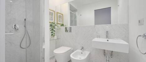 A modern bathroom with a glass-enclosed shower, a bidet, a sink, and a mirror.