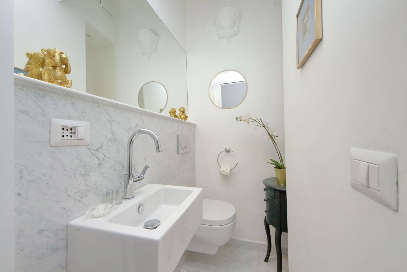 A bathroom with a white sink, a toilet, and a mirror. There is a gold statue on the countertop, a potted plant, and a framed picture on the wall.