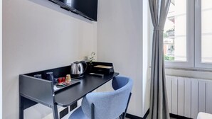 Ein modernes Zimmer mit einem schwarzen Schreibtisch, einem blauen Stuhl, einem Wand-Fernseher und einem Fenster mit Vorhängen.
