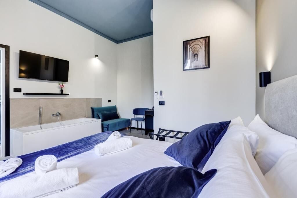 A hotel room with a bed, a desk, a chair, a TV mounted on the wall, and a bathroom with a bathtub and sink.