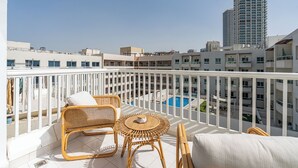 Ein Balkon mit Korbmöbeln, einem Pool und Hochhäusern im Hintergrund.