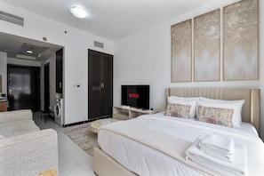 A modern hotel room with a bed, a TV, a wardrobe, and a seating area. - Beautiful Studio in JVC near Halfa Park (Dubai)