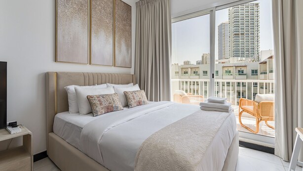 Ein modernes Hotelzimmer mit einem großen Bett, einem Flachbildfernseher, einem Balkon mit Korbstühlen und Blick auf die Stadt.