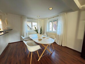 A dining area with a round table, white chairs, and a potted plant.