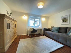 A living room with a sofa, a chair, a window with curtains, a radiator, and a cabinet.