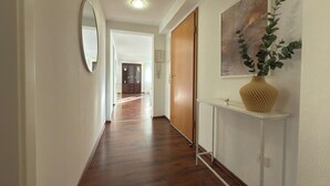 A hallway with wooden flooring, a white console table with a vase, a mirror, and a painting on the wall. - Scharnhäusle 2- Large apartment with bathtub & balcony (Ostfildern)