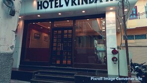 Das Hotel VRINDA von außen, mit einem markanten Eingang, einer Glastür und einer Treppe, die zum Eingang führt.