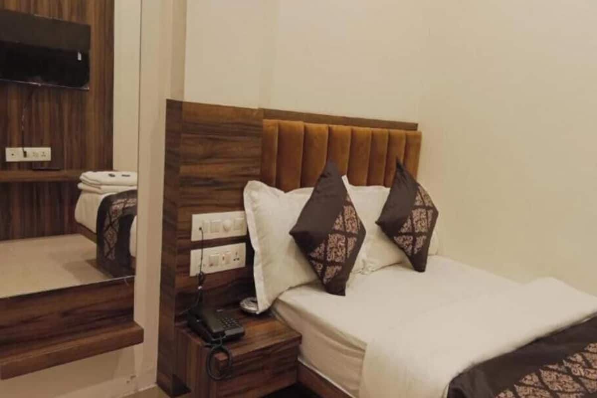 A hotel room with a wooden headboard, a bed with white and patterned pillows, a bedside table with a remote control, and a TV mounted on the wall.