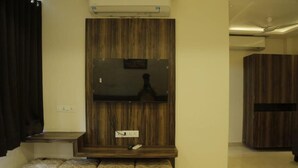 Ein Zimmer mit einem Holzschrank, einem flachbildfernseher an der Wand und einer Sitzbank mit gemusterten Kissen.