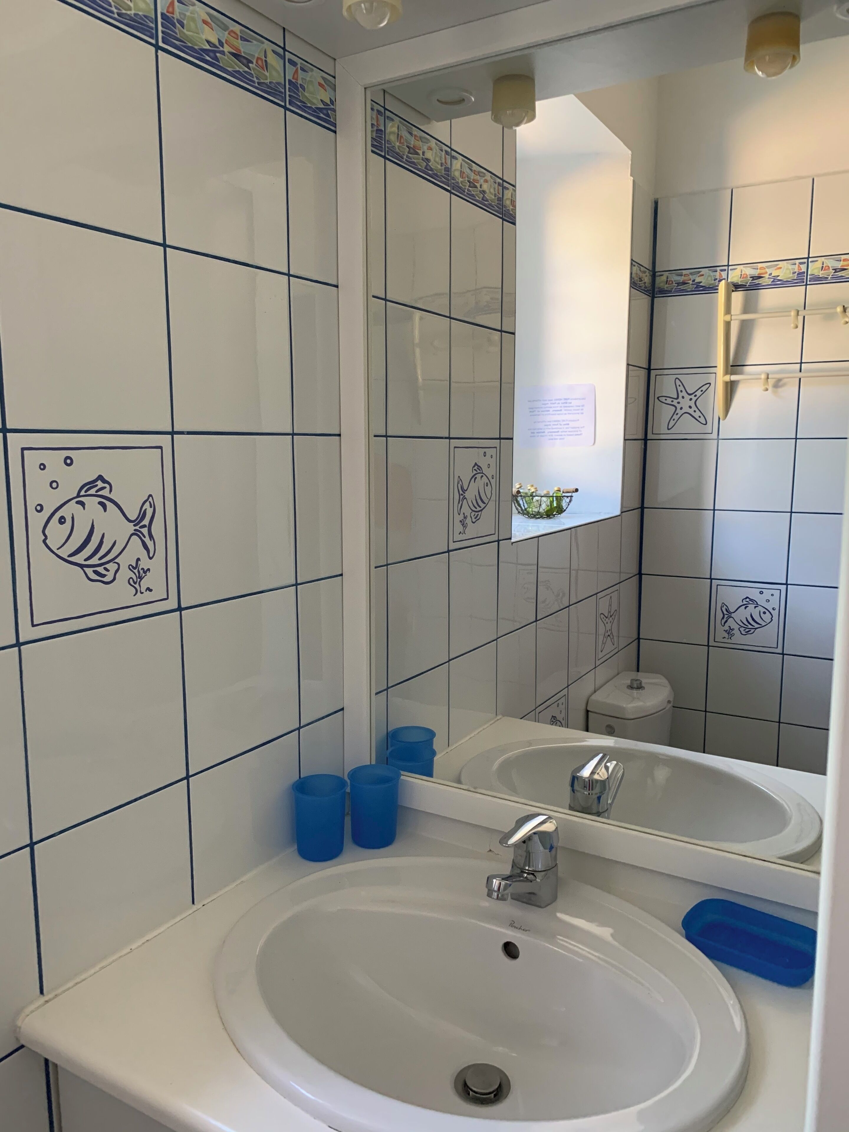 A bathroom with white tiles, fish designs, a sink, and a mirror.