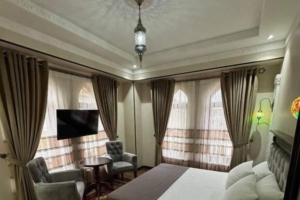 A hotel room with a large bed, a TV, a desk with two chairs, and a patterned rug.