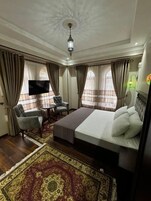 A hotel room with a large bed, a TV, a desk with two chairs, and a patterned rug.