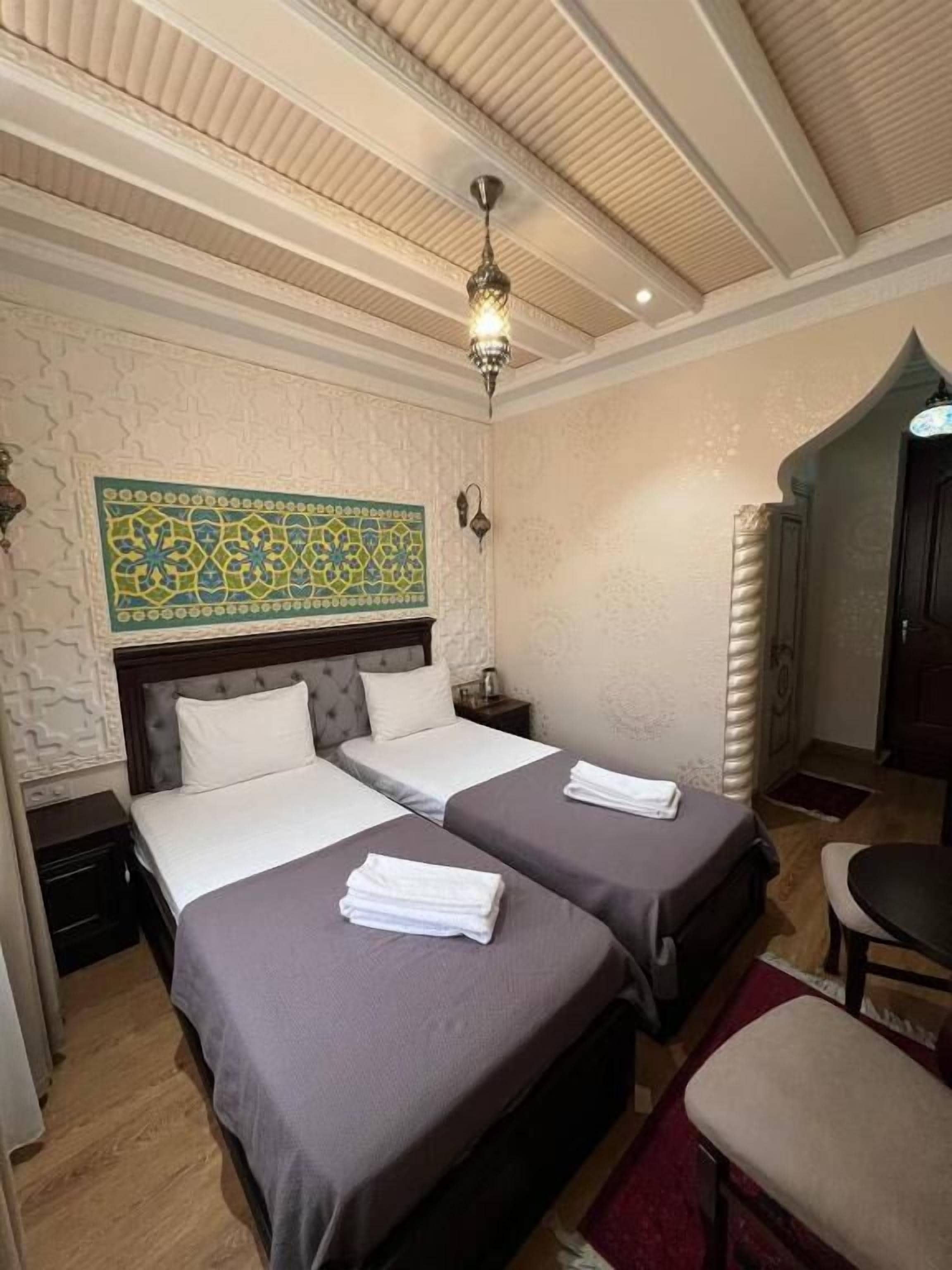 A hotel room with two beds, a chandelier, a decorative wall hanging, and a small seating area.