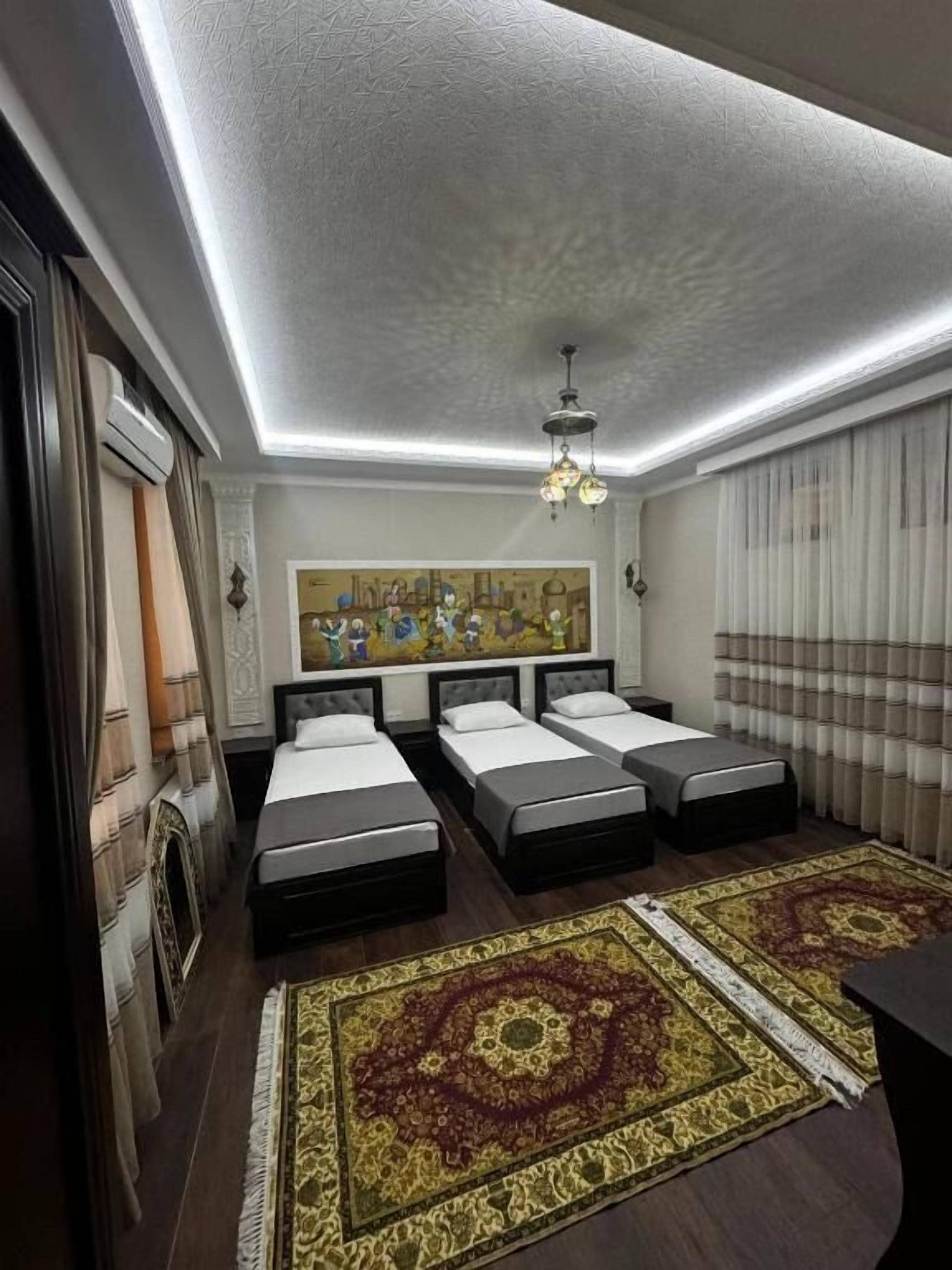 A hotel room with three beds, a large painting, a chandelier, and a patterned rug.