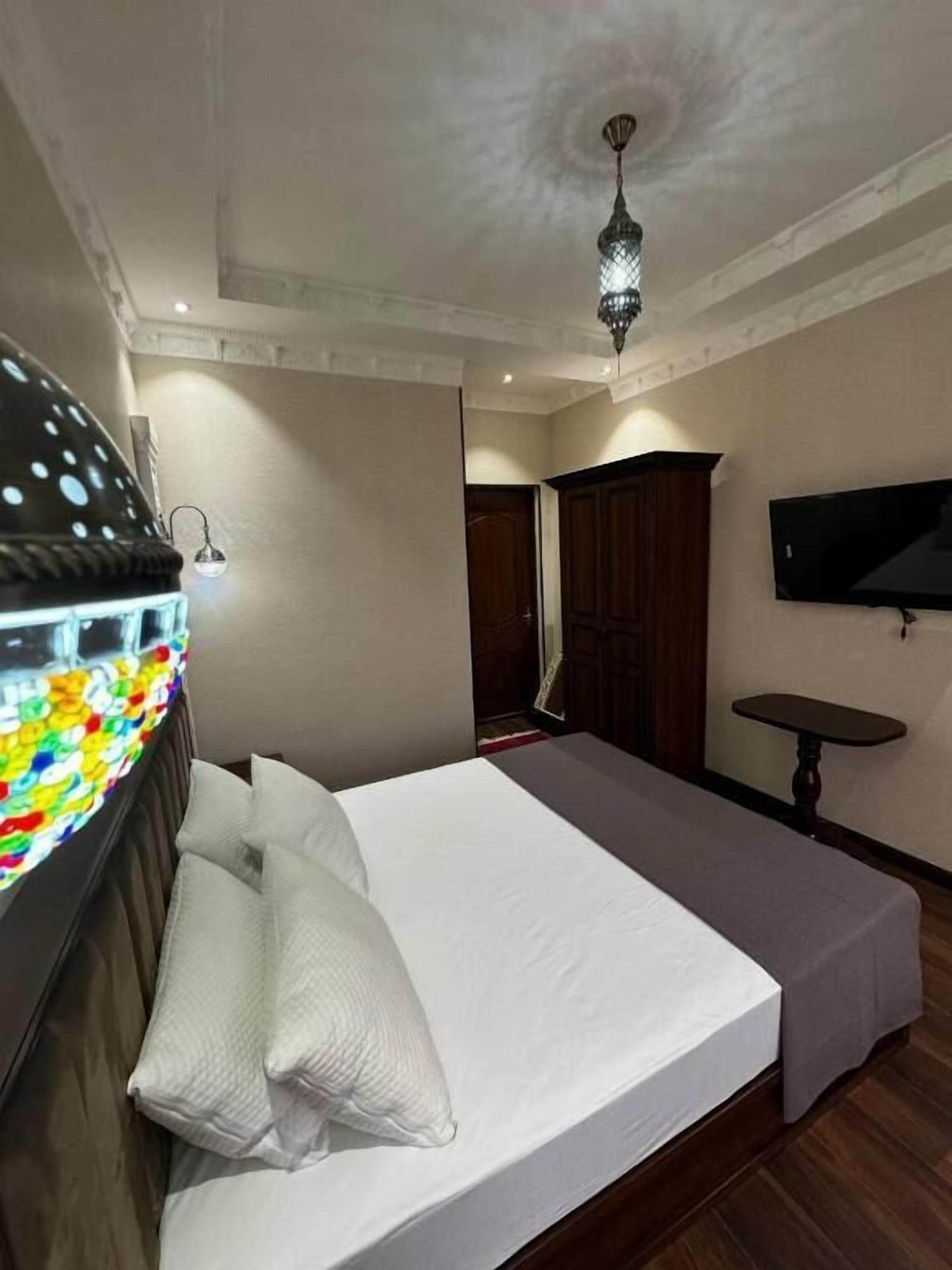 A bedroom with a bed, a nightstand, a TV, and a ceiling light.