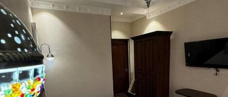 A bedroom with a bed, a nightstand, a TV, and a ceiling light.