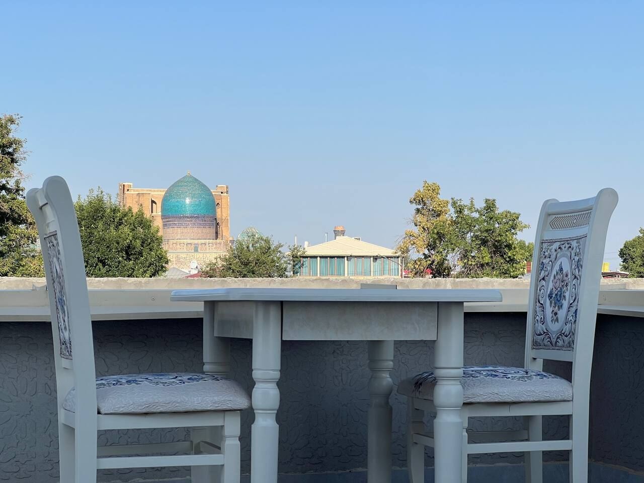 A terrace with two white chairs and a table, overlooking a building with a dome and a smaller structure.