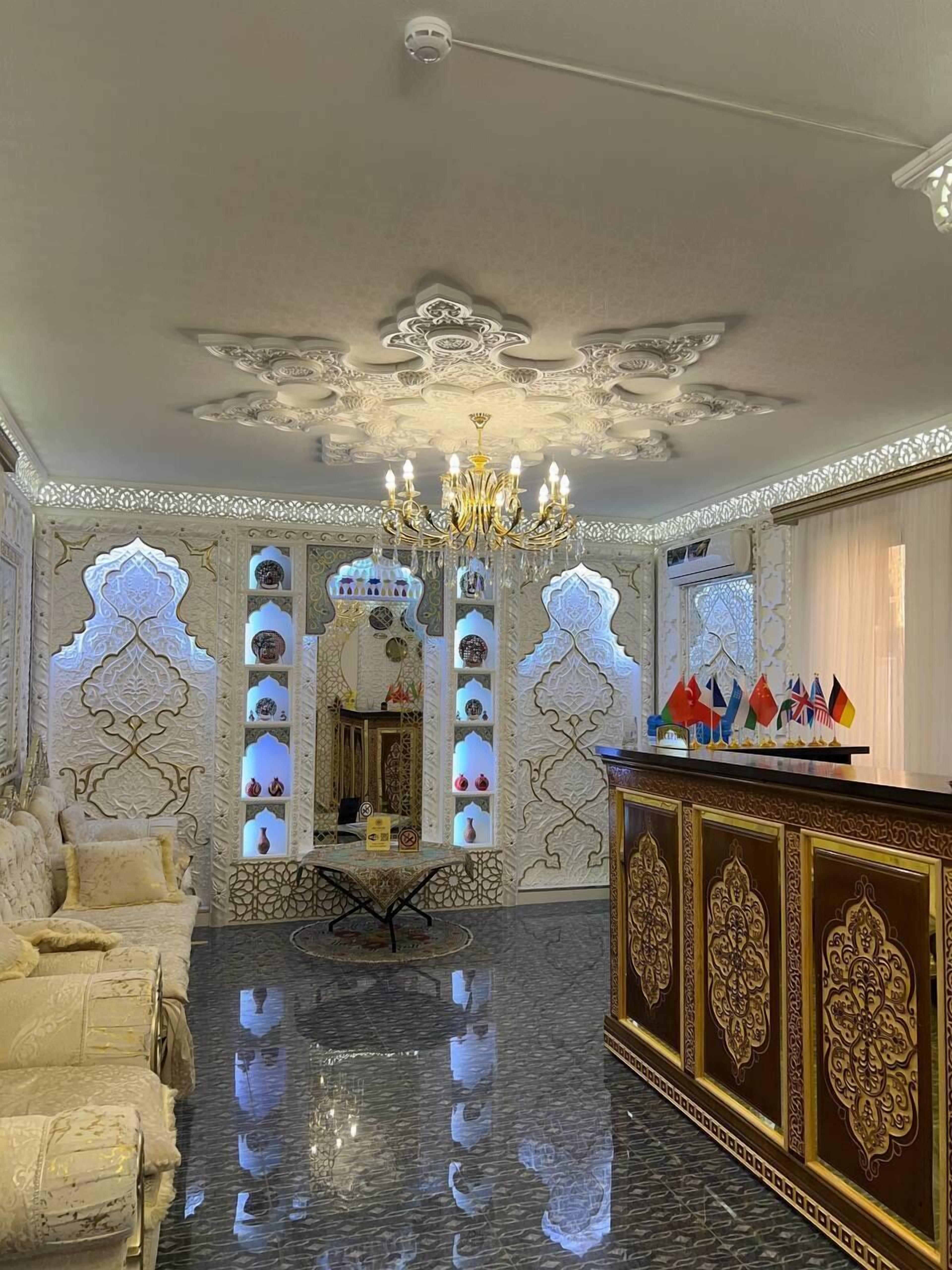 A luxurious lobby with ornate wall designs, a chandelier, and a reception desk with flags.