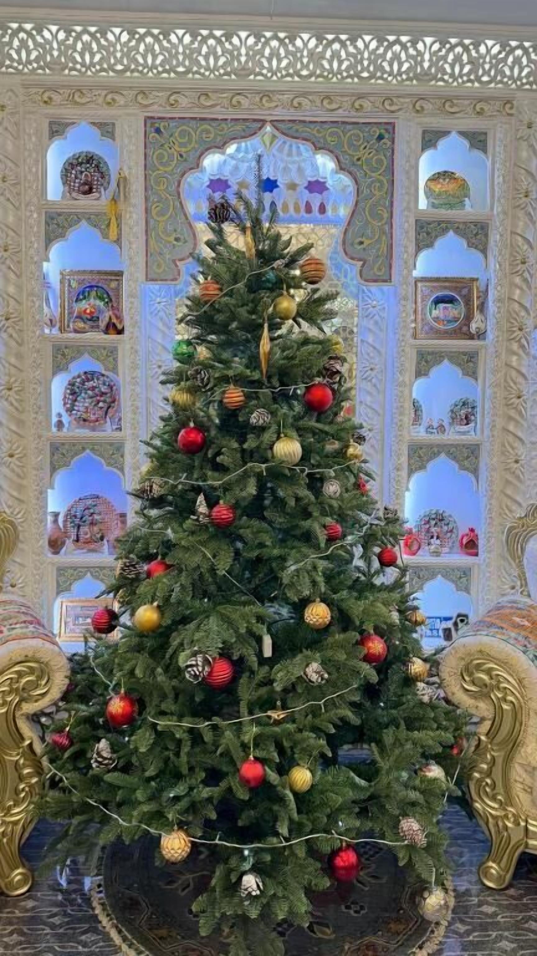 A Christmas tree decorated with ornaments, set against a backdrop of ornate architectural details.