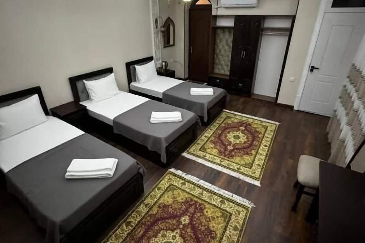A hotel room with three single beds, a desk, a chair, a ceiling fan, and patterned rugs.