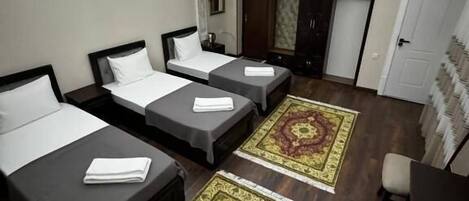 Ett hotellrum med tre enkelsängar, ett skrivbord, en stol, en takfläkt och mönstrade mattor.