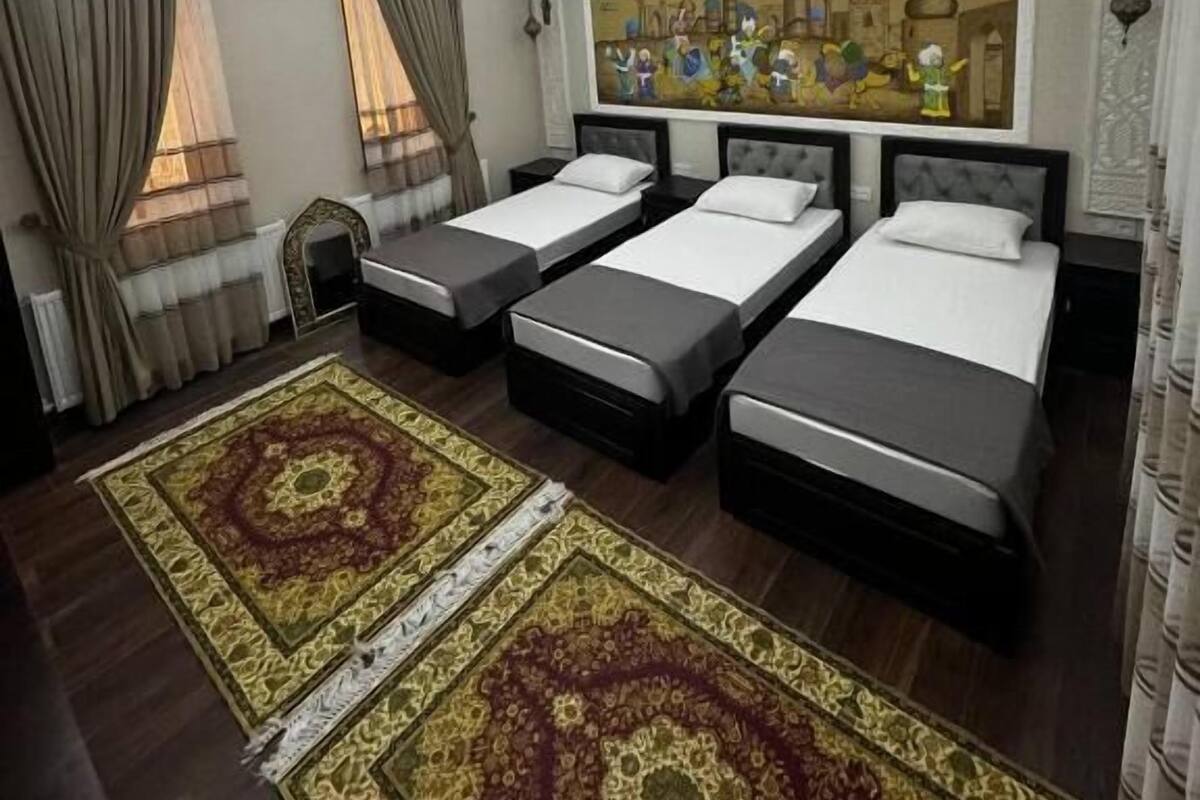 A hotel room with four single beds, a large painting on the wall, a ceiling light fixture, and a patterned rug on the floor.