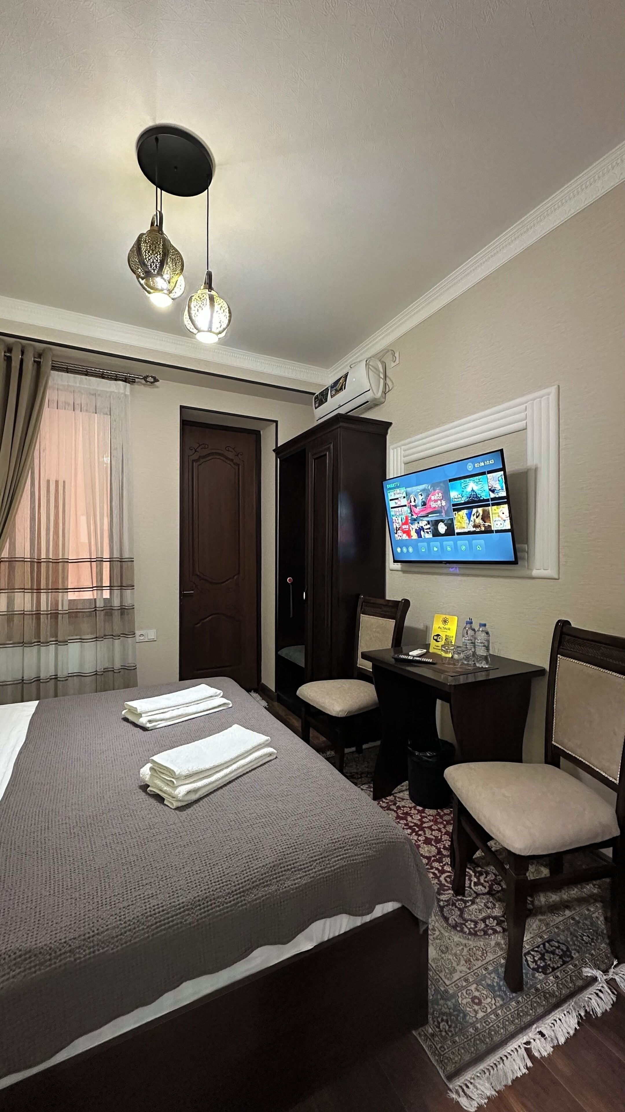 Una habitación de hotel con cama, escritorio con silla, televisor y ventana con cortinas.