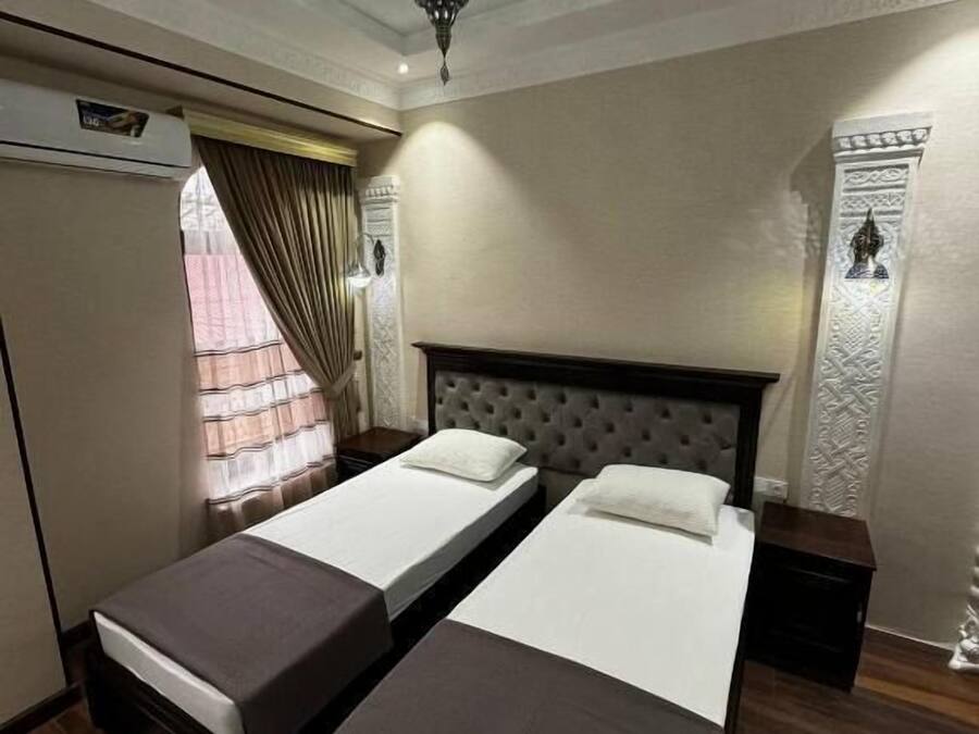 A hotel room with two single beds, a large mirror, a wardrobe, and a decorative wall panel.