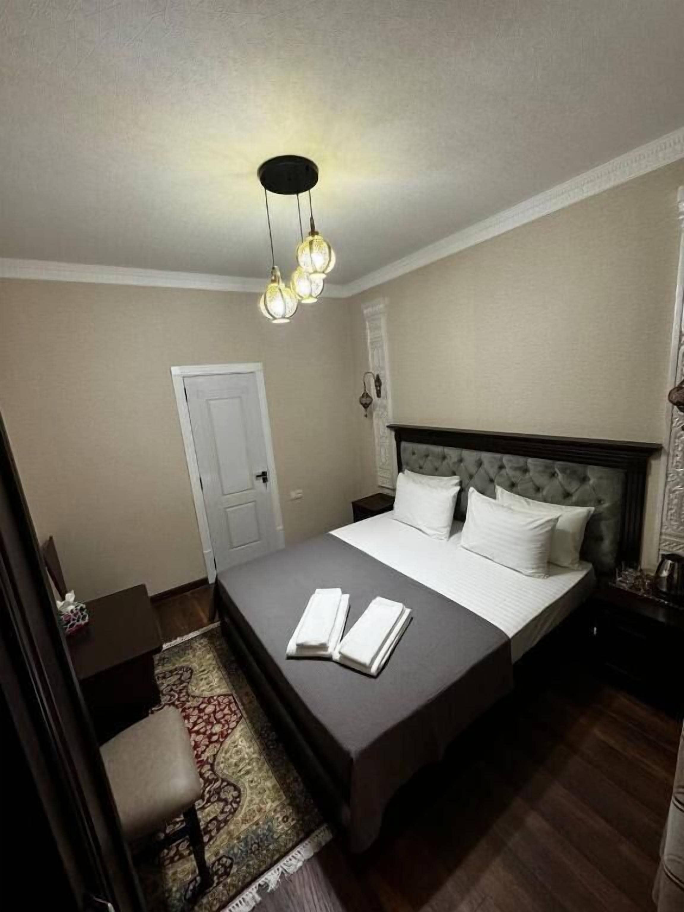 Habitación de hotel ordenada con una cama grande, una mesita de noche, una silla y una alfombra estampada.