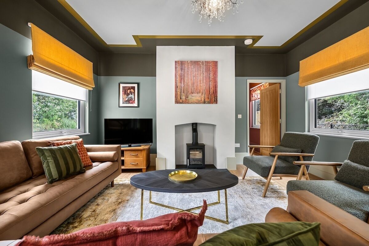 Ein modernes Wohnzimmer mit einer Couch, Sesseln, einem runden Couchtisch, einem Kamin und einem Fernseher.