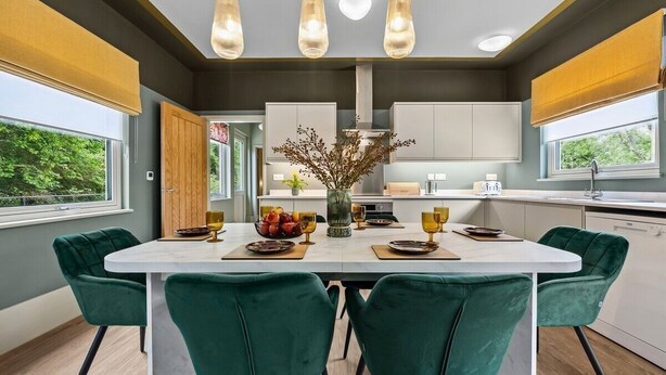 Une cuisine moderne dotée d’un îlot central, de luminaires suspendus et offrant une vue sur l’extérieur.