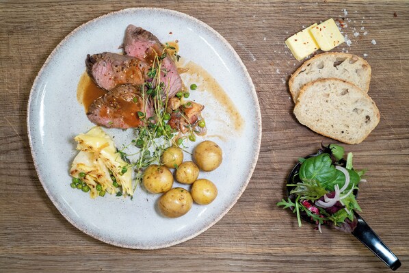 Une assiette de nourriture comprenant de la viande, des pommes de terre et du pain, posée sur une table en bois.