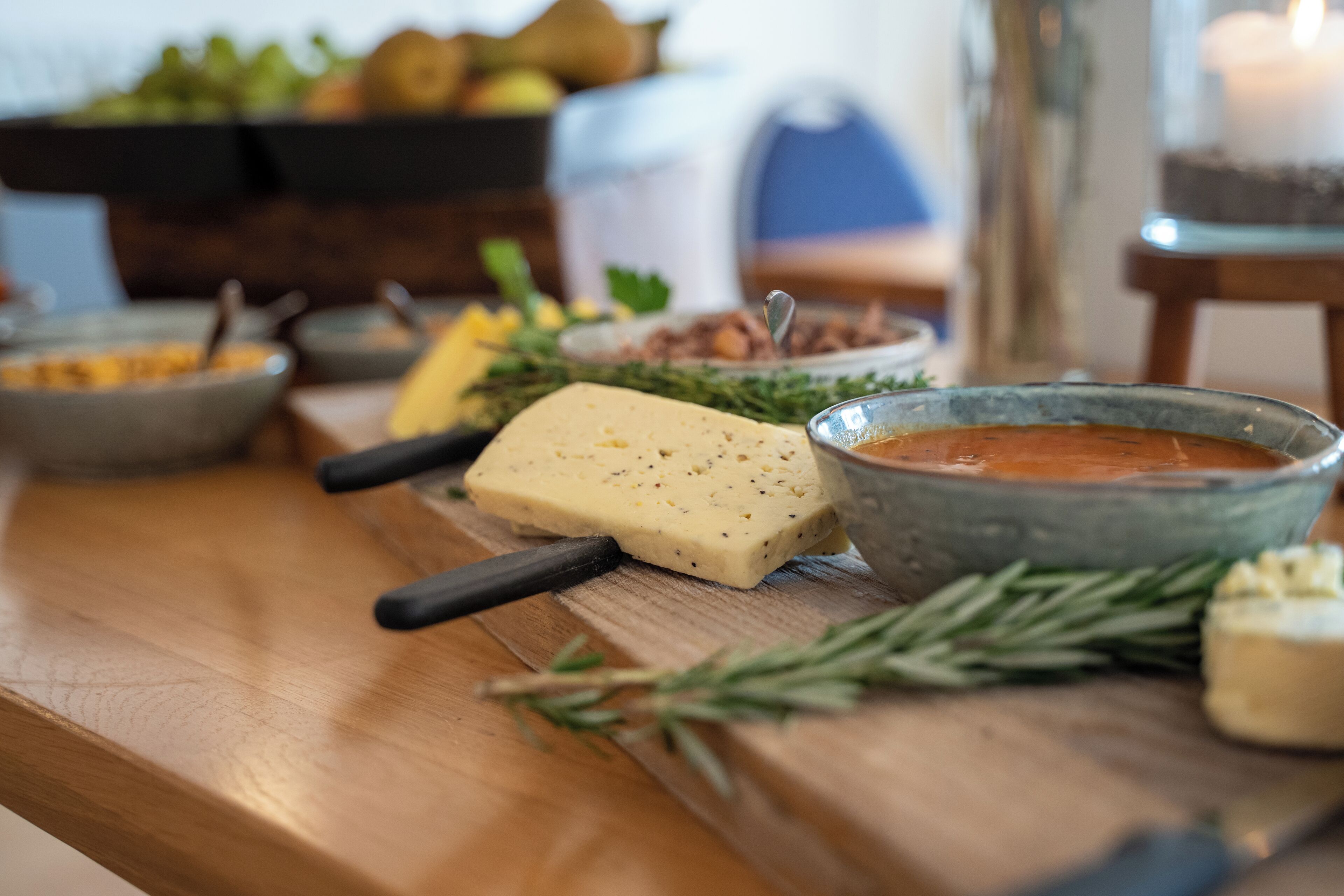 A wooden table with a cheese, a bowl of sauce, and some herbs.
