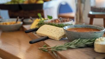 A wooden table with a cheese, a bowl of sauce, and some herbs.