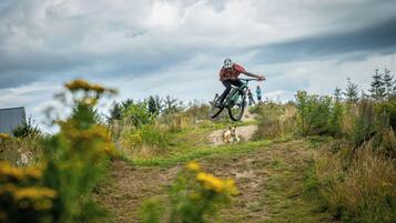 Una persona en una bicicleta de montaña sobre un sendero de tierra con vegetación y un cielo nublado.
