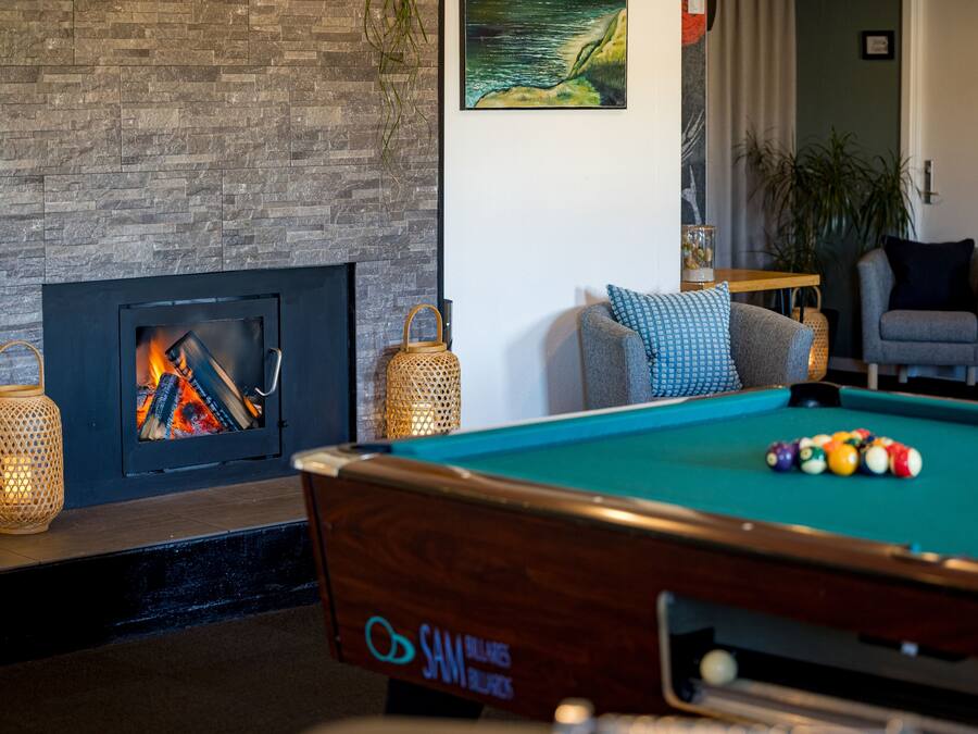 A pool table with balls, a fireplace with logs, and a lounge chair.