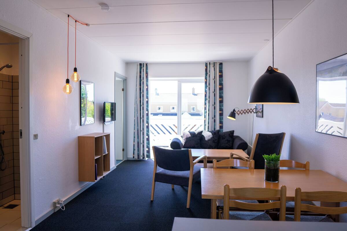 Une chambre d’hôtel moderne dotée d’un coin repas, d’un canapé et d’une grande fenêtre avec des rideaux.