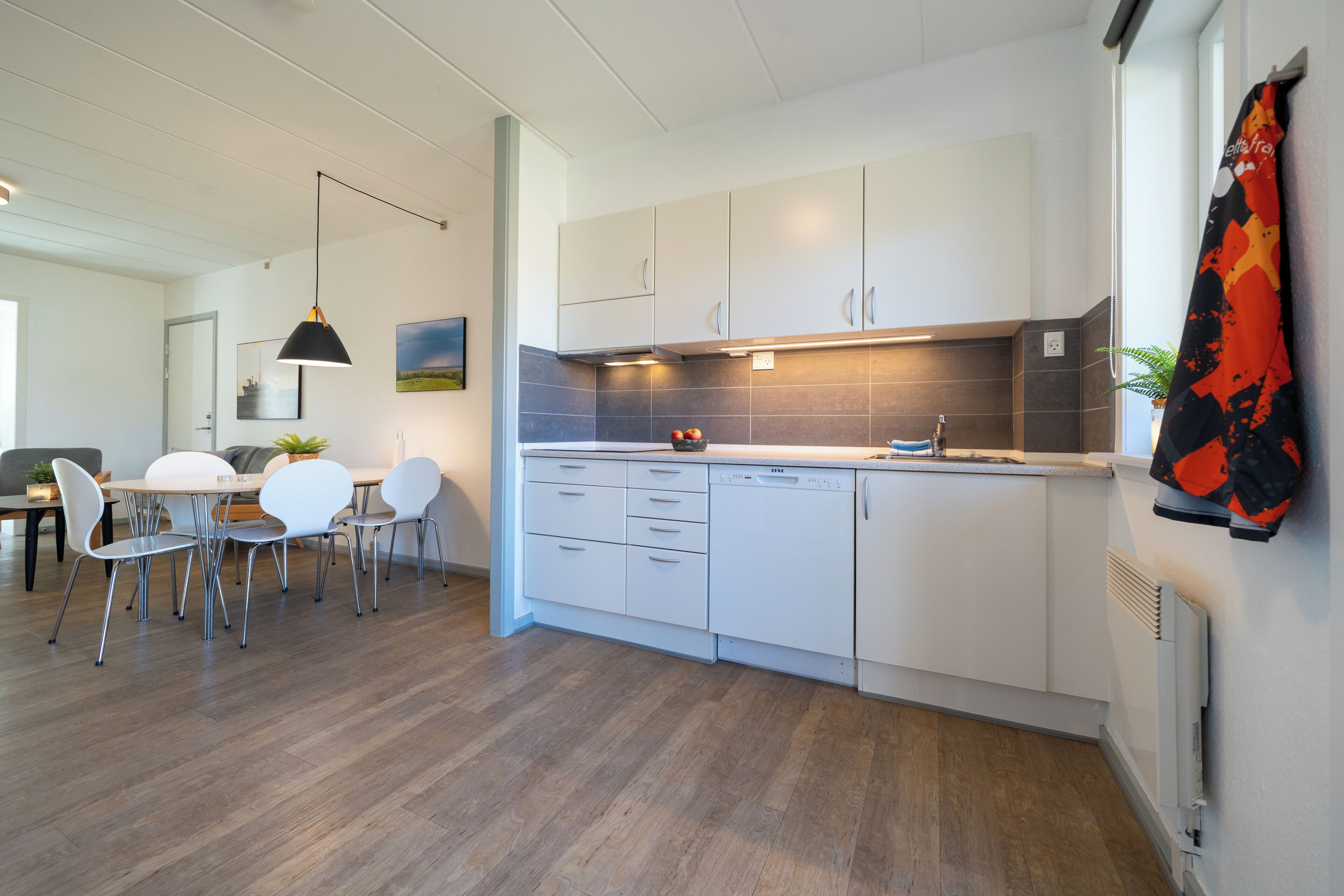 A modern kitchen with white cabinets, a dishwasher, and a dining area with white chairs and a table.