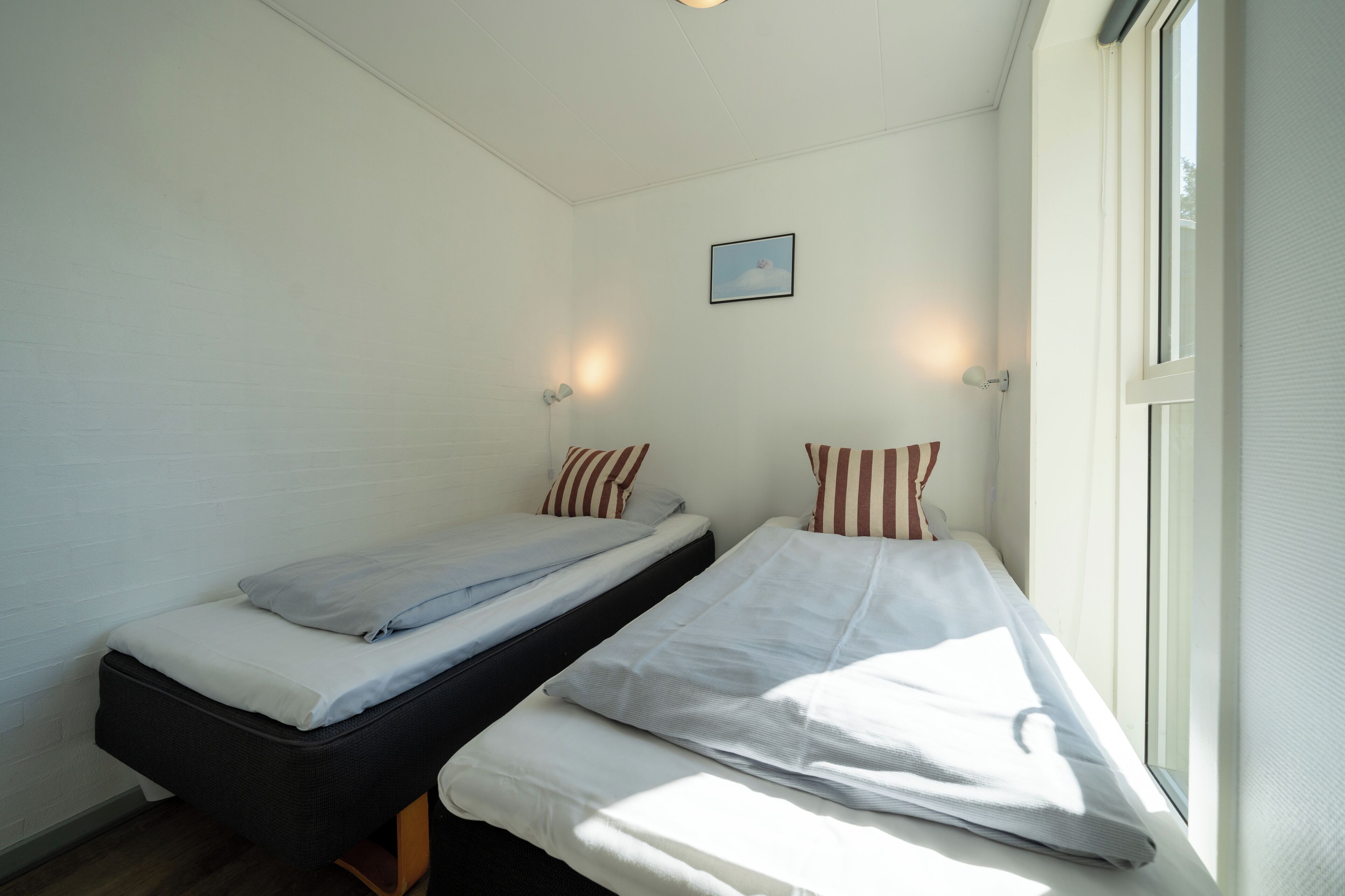 A room with two beds, a small window, and a wall-mounted picture.