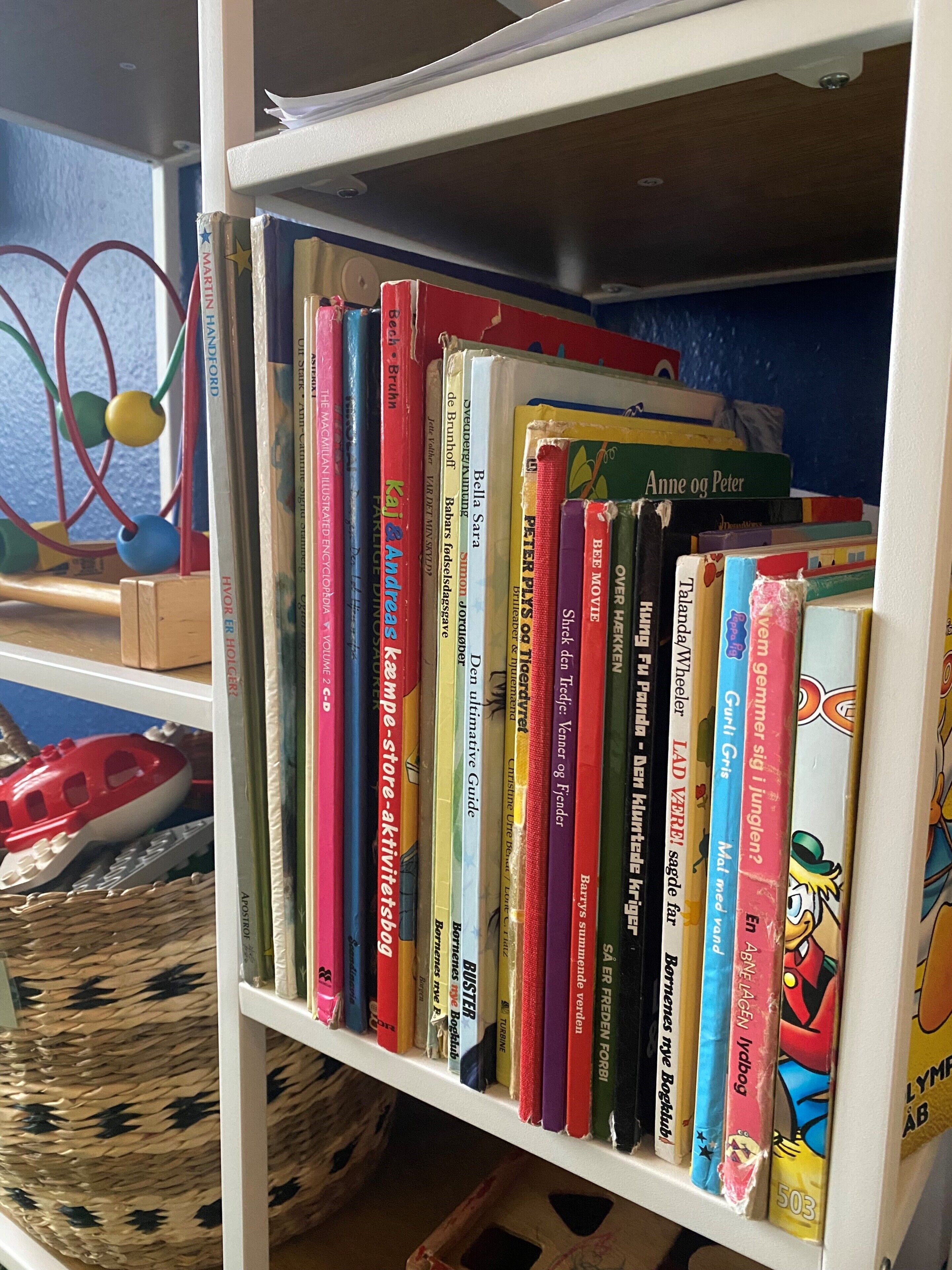 A bookshelf with various books, a woven basket, and a toy car.