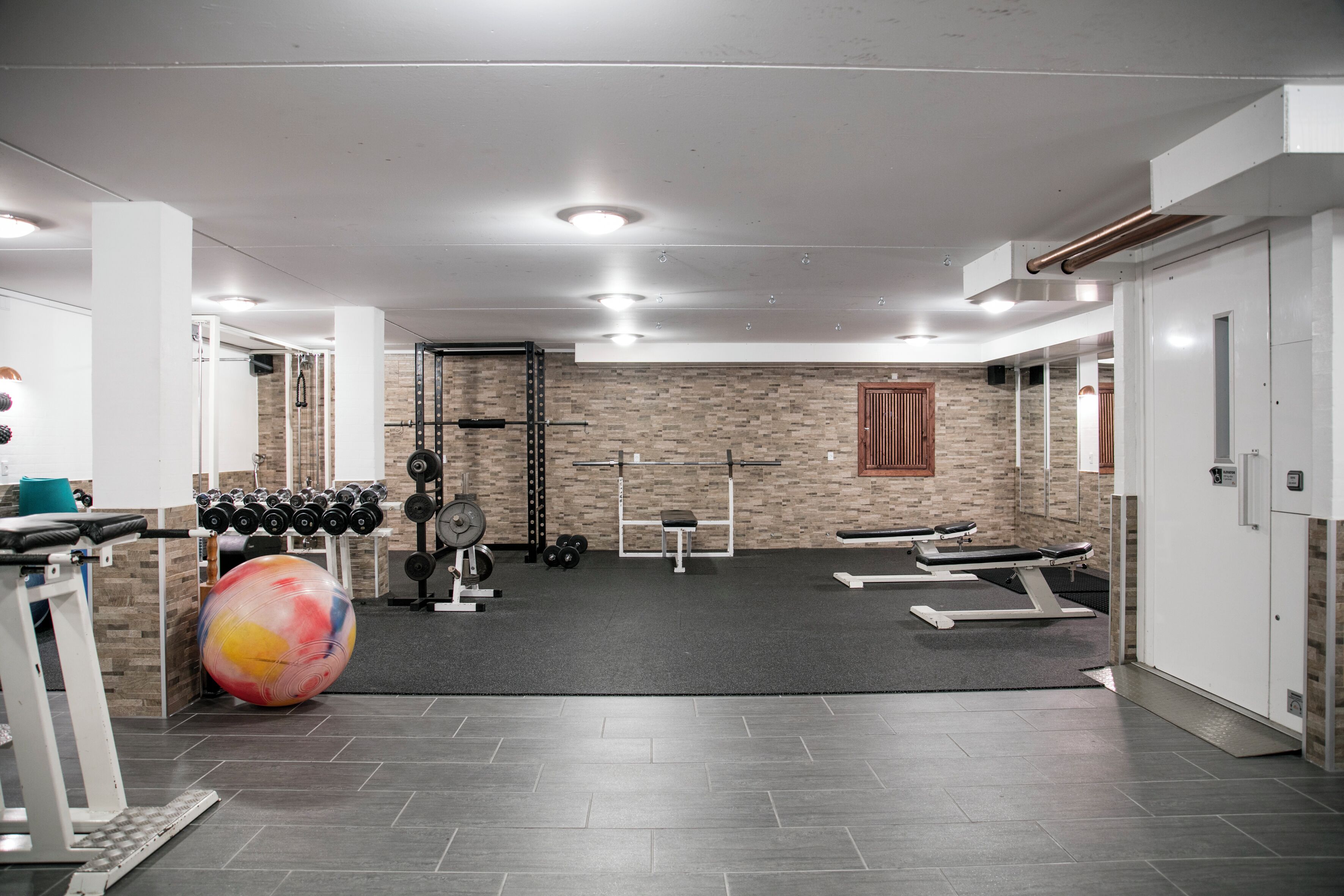 Un gimnasio con equipamiento de ejercicio, una pelota grande y una pared de ladrillo.