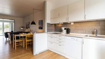 Eine moderne Küche mit weißen Schränken, einem Geschirrspüler, einer Kaffeemaschine und einem Essbereich mit Tisch und Stühlen.