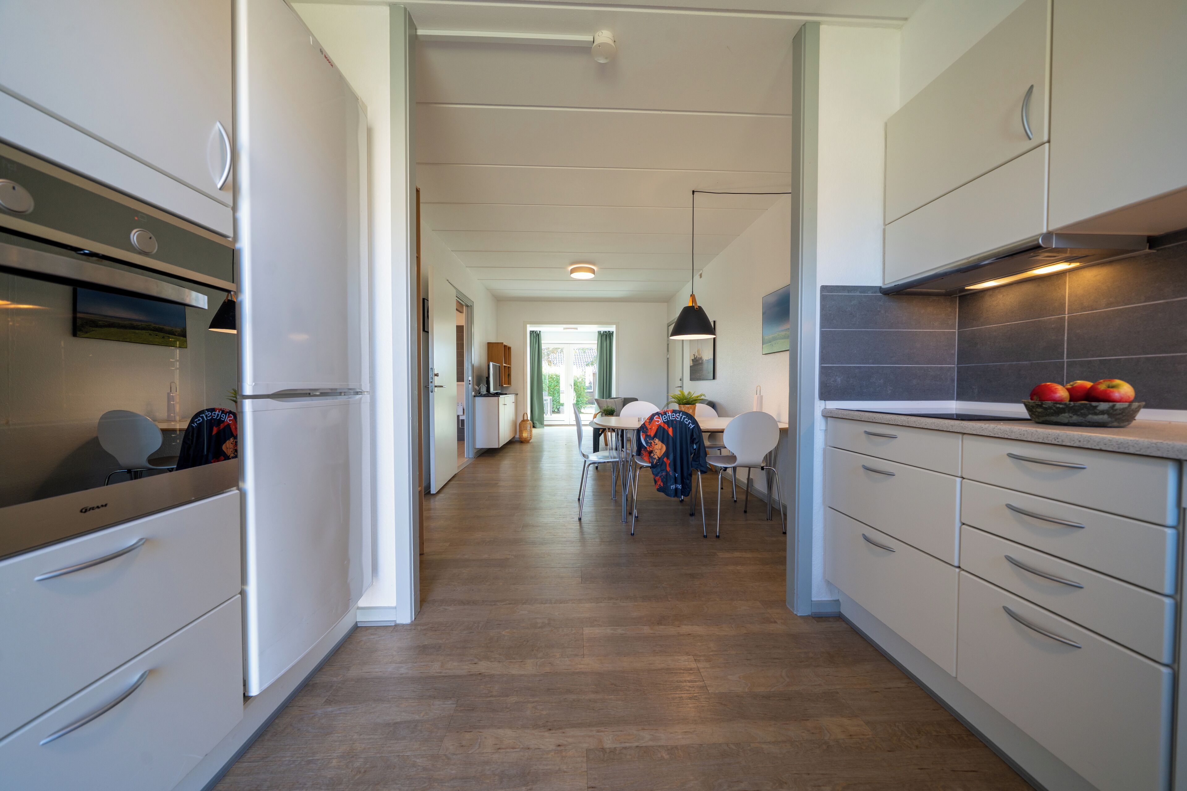 A modern kitchen with white cabinetry, a dining area with a table and chairs, and a hallway leading to an open space.